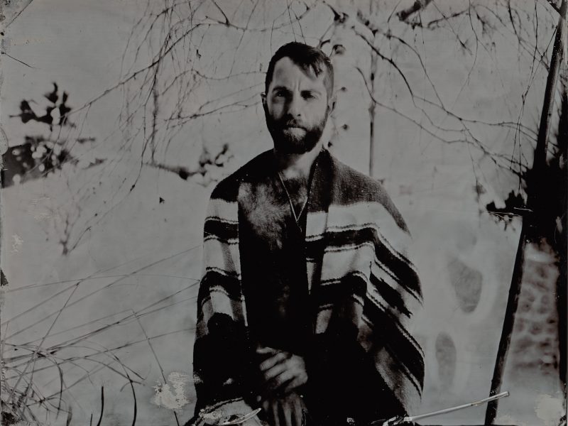 A shirtless man covered with blanket sits in snow