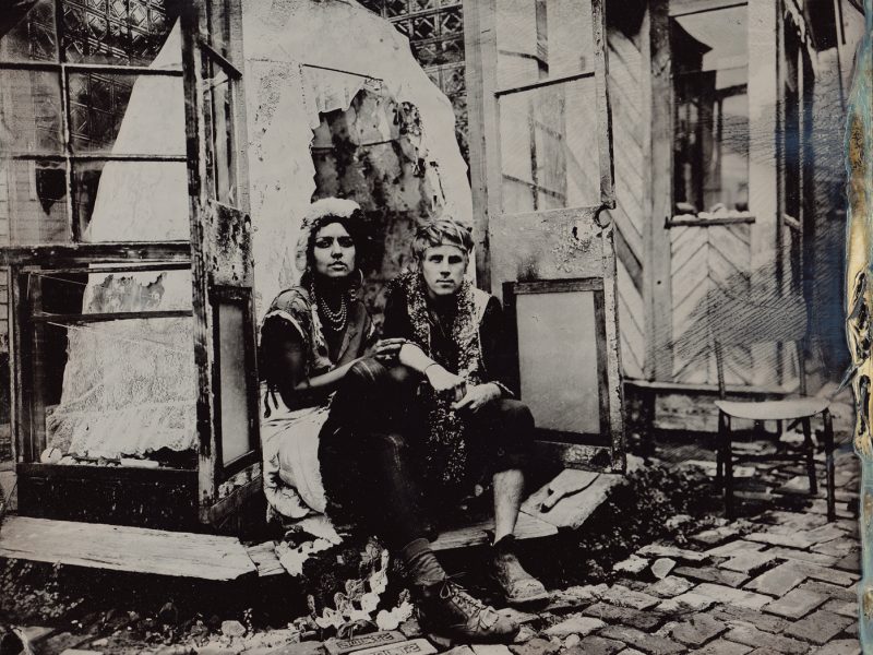 Two people sitting in a glass doorway infront of a lace bell
