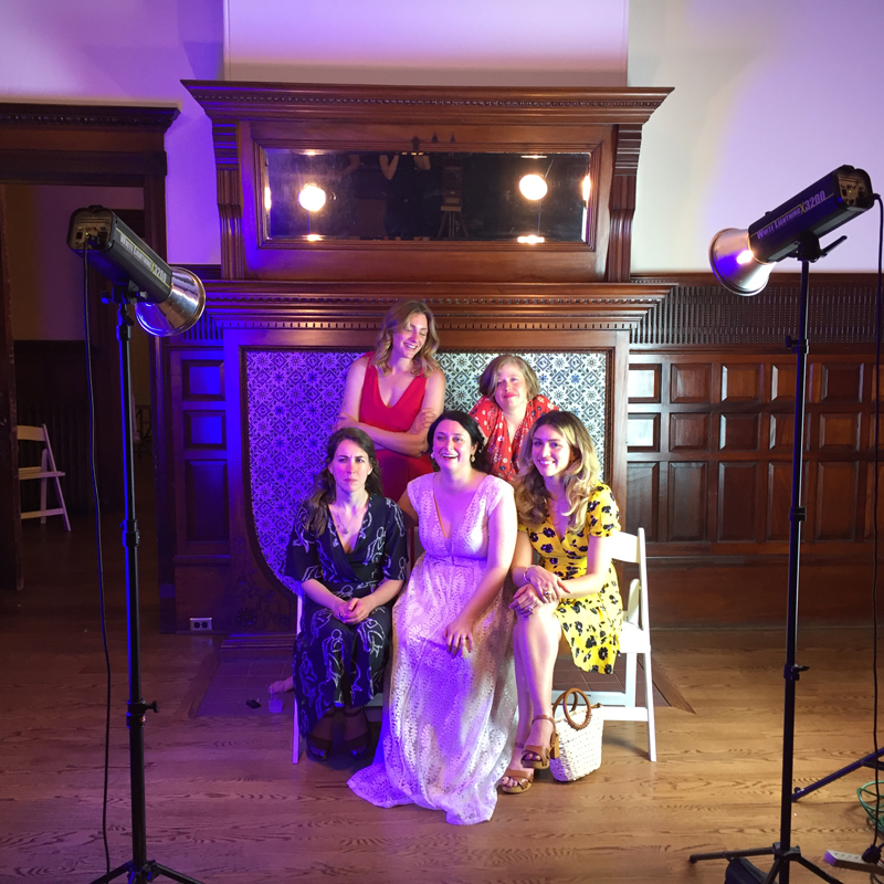 A bride and four friends smile broadly infront of studio lights. One light is casting a purple glow.