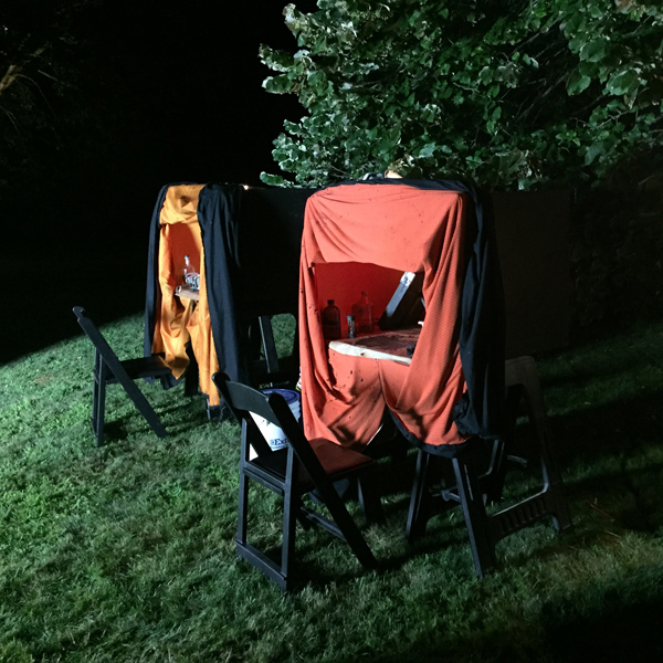 Two portable darkrooms are set up outdoors at night with light shining on them from one side.