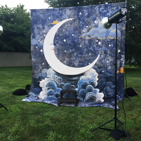 A paper moon set outdoors in a grassy field with studio lights nearby.