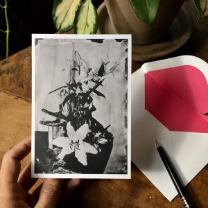 Notecard with alligator head and white lilies in front of white envelope with pink lining and pen
